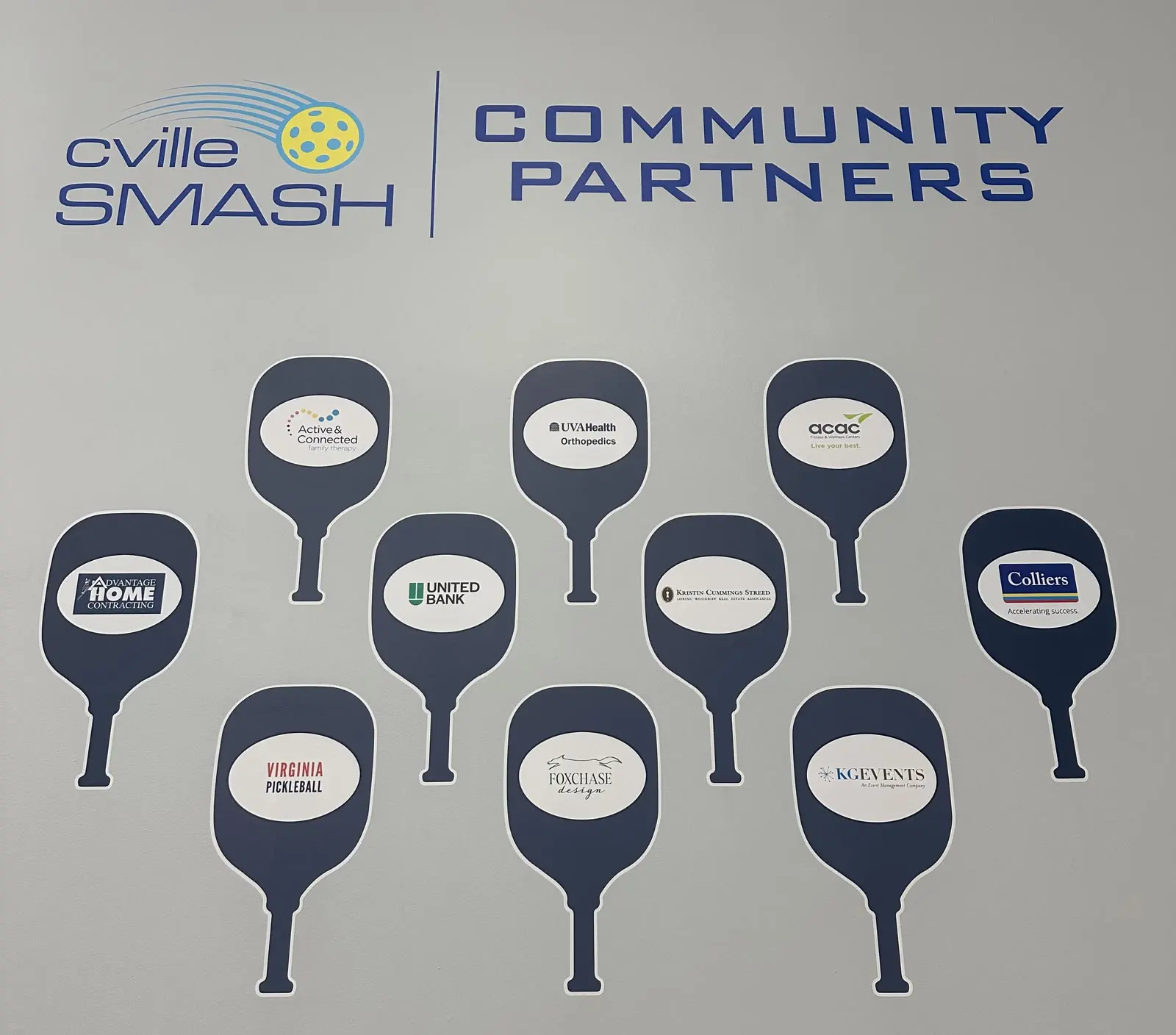 The Community Partners wall at cvilleSMASH, with each partner's logo on a paddle